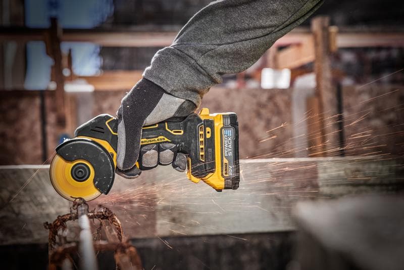 A close-up of a person using a yellow and black DEWALT cordless brushless power tool, cutting through a metal rod with sparks flying.