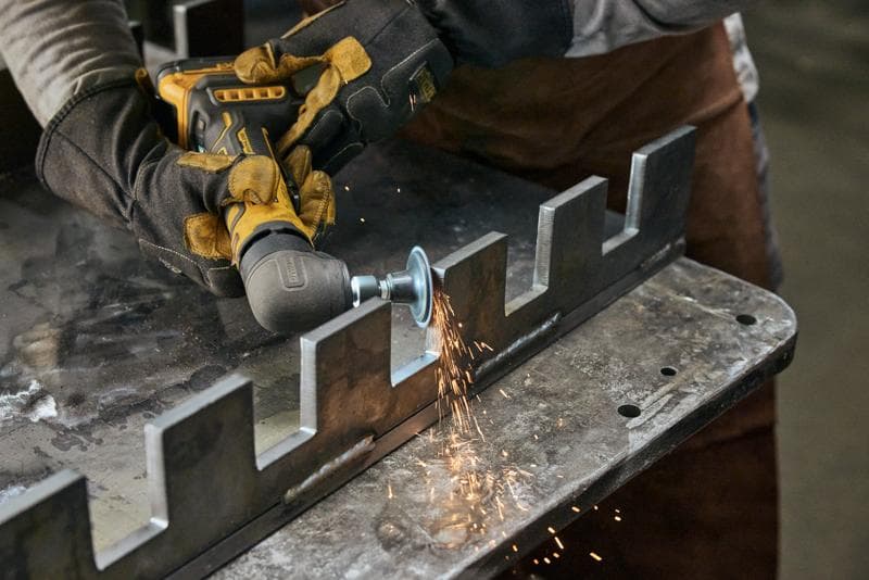 A person wearing protective gloves uses a DEWALT cordless angle grinder to grind the edge of a metal workpiece, producing sparks.