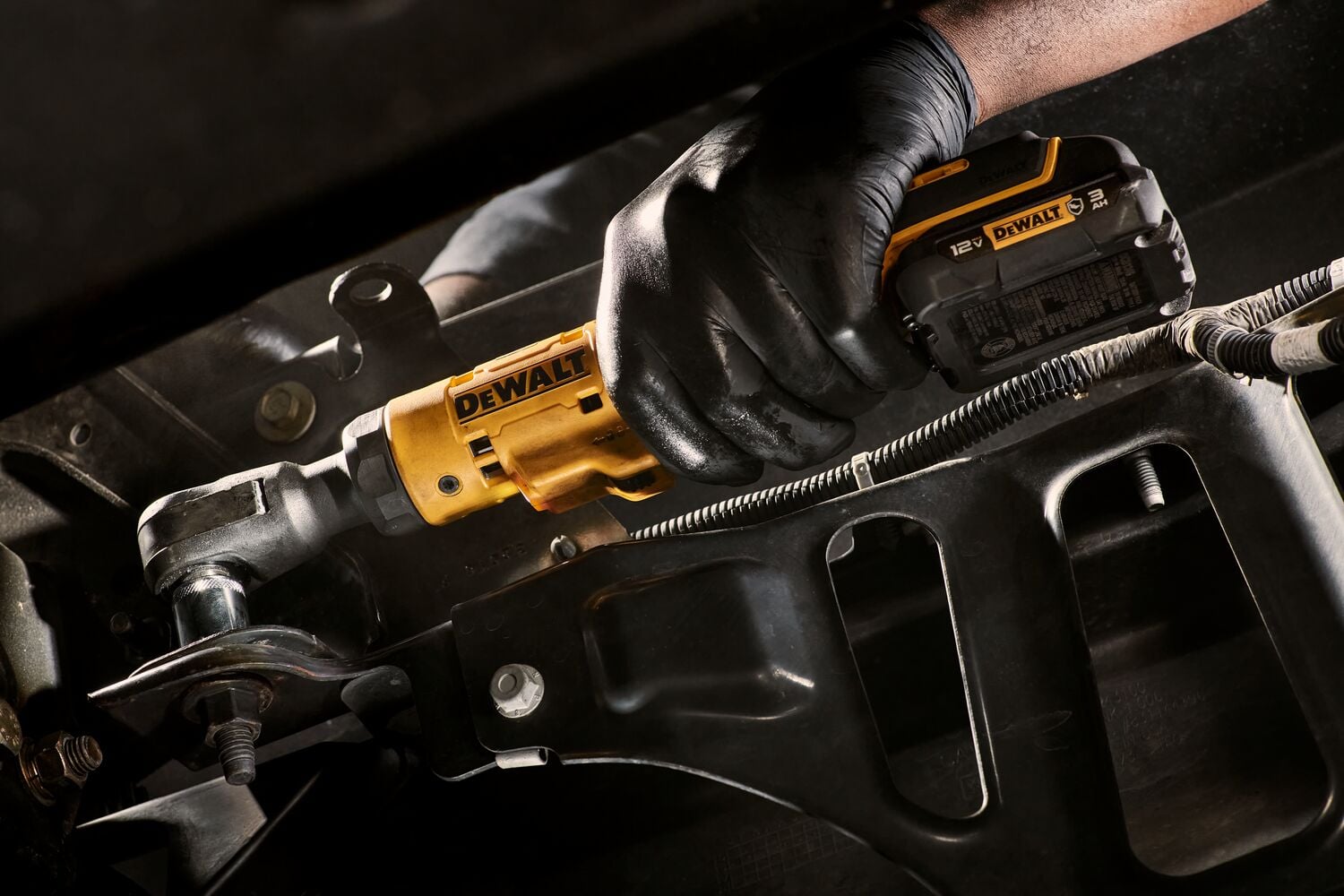 A gloved hand operating a DEWALT DCF503B cordless ratchet wrench, tightening a bolt on a metal component in an industrial or automotive setting.