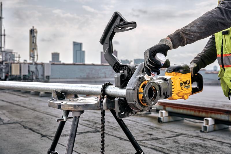 A person using a DEWALT pipe threading machine on a metal pipe outdoors, with city buildings visible in the background.