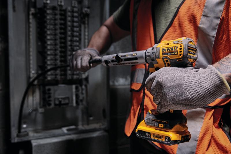 A person wearing an orange safety vest and gloves uses a DEWALT cordless tool to work on electrical cables beside a panel.