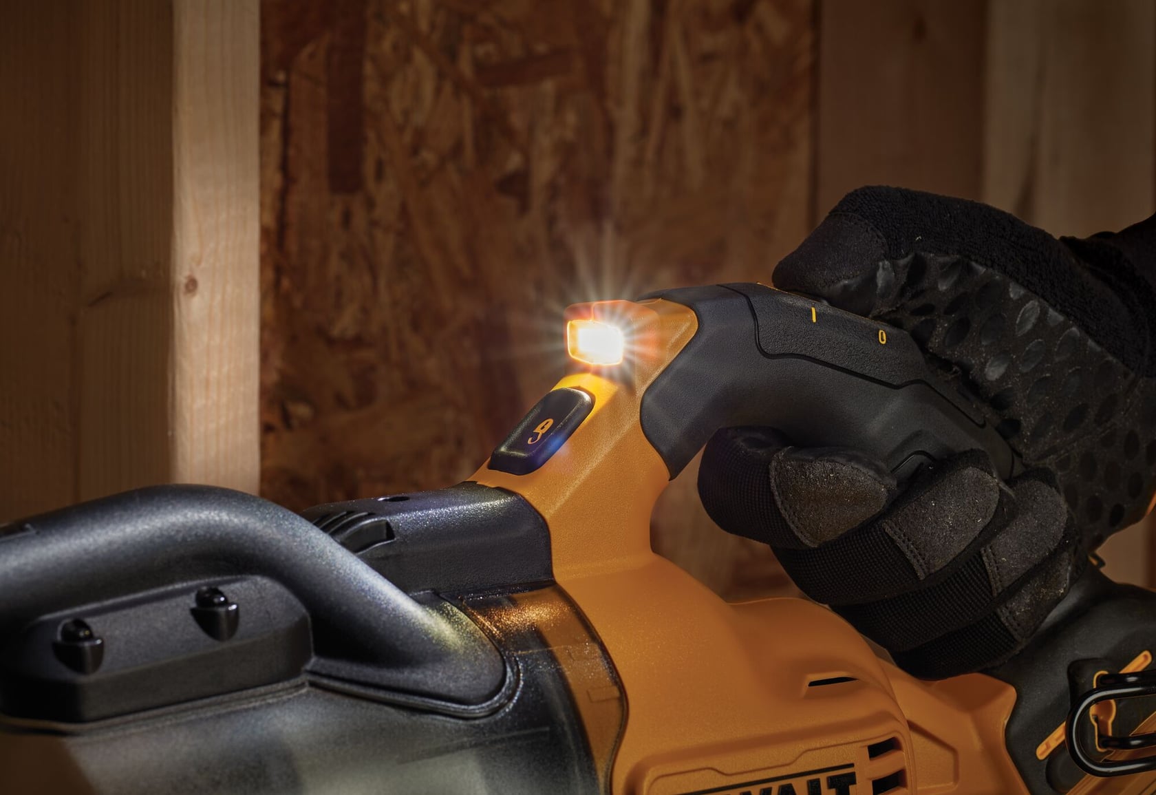 Close-up of a gloved hand operating a yellow and black DEWALT power tool with a built-in LED light illuminated, in a workshop setting.