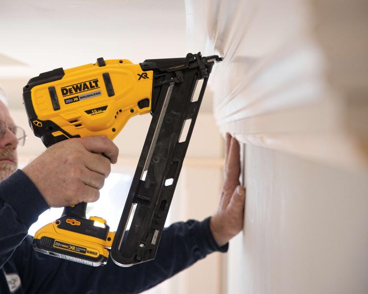 A person using a DEWALT 20V XR brushless cordless nailer to attach molding to a wall.