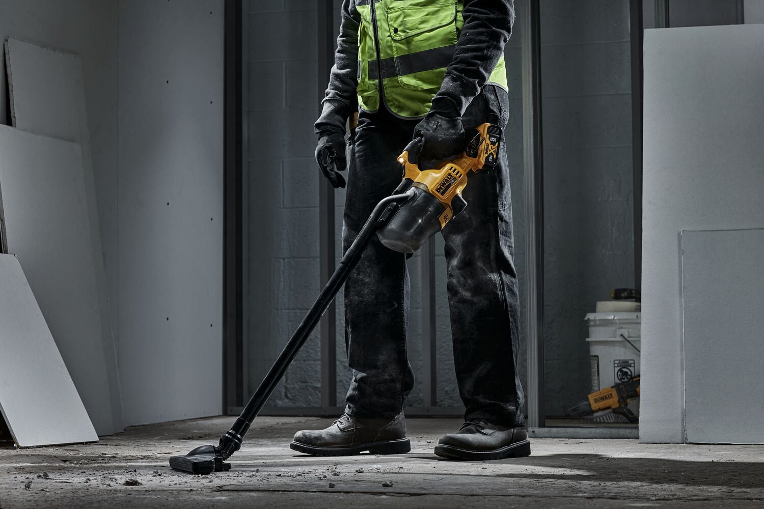 Male using DEWALT 20 MAX* Hand Vacuum with extension tube and floor nozzle accessories vacuuming up drywall, dust, and small screws on a jobsite. DEWALT 5AH hour battery is being used. LED light is powered on.