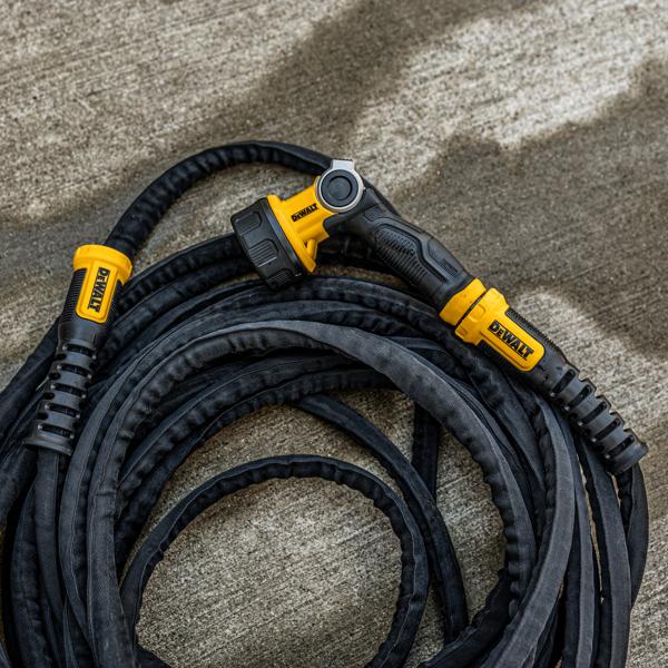 A coiled DEWALT heavy-duty garden hose with a black and yellow spray nozzle attachment lying on a concrete surface.