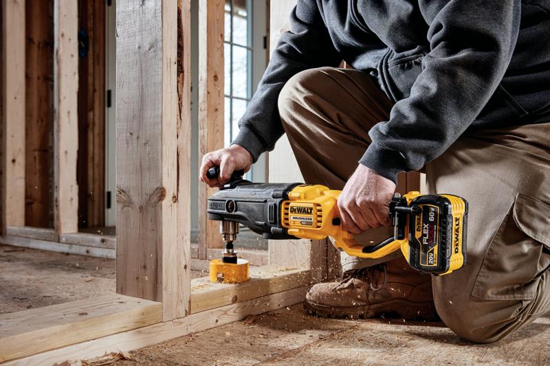 A person using a DEWALT DCD470X1 cordless power drill with a hole saw attachment to drill into a wooden beam at a construction site.