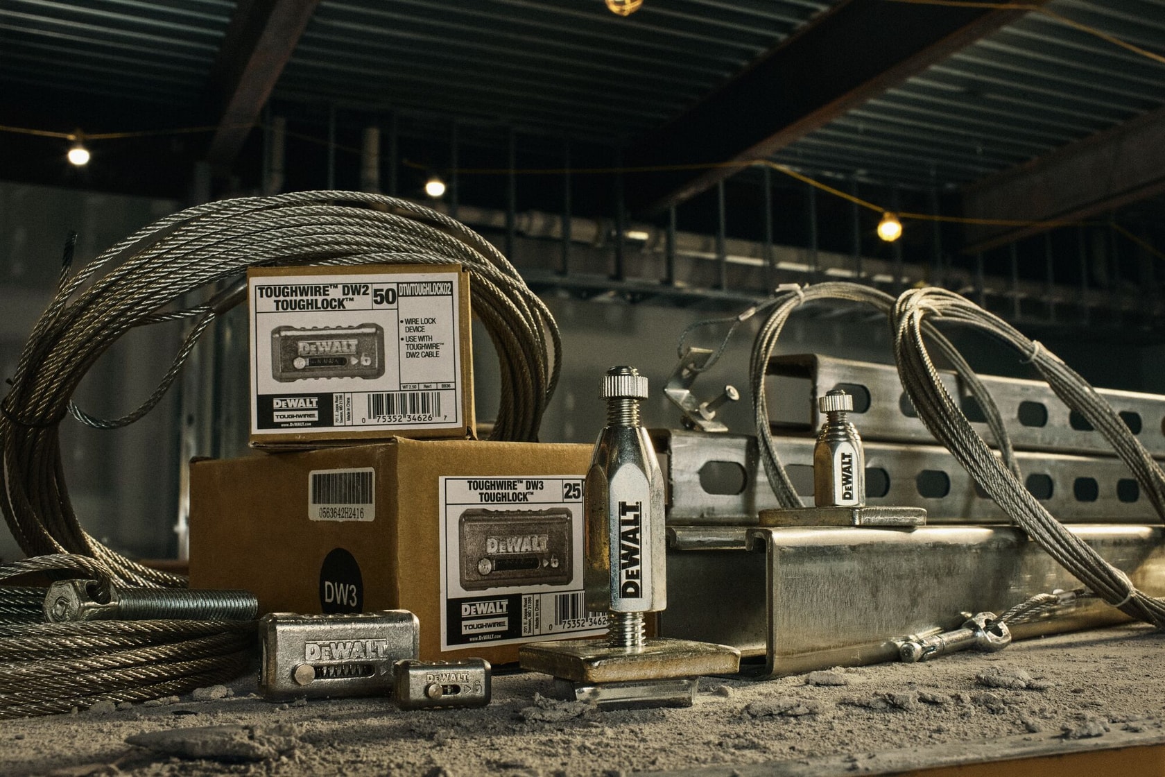 DEWALT Toughwire and Toughlock products displayed on a dusty metal surface, including steel wire cables, locking mechanisms, boxes with product labels, and some metal construction components in an industrial workshop setting.