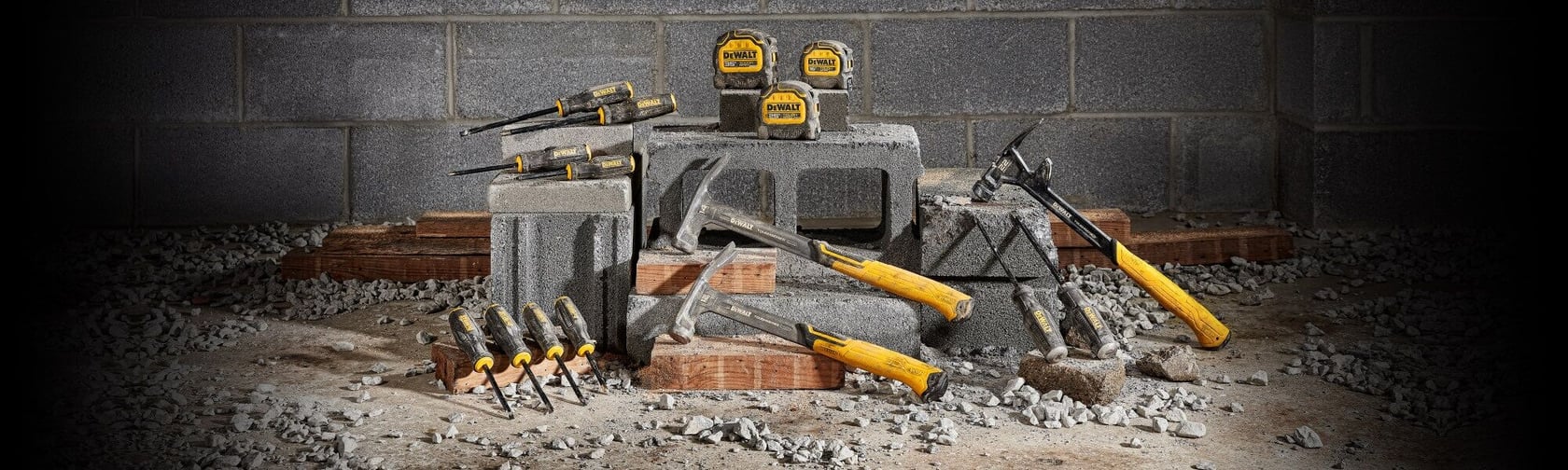 A collection of DEWALT hand tools including hammers, screwdrivers, and tape measures displayed on concrete blocks in a construction site setting.
