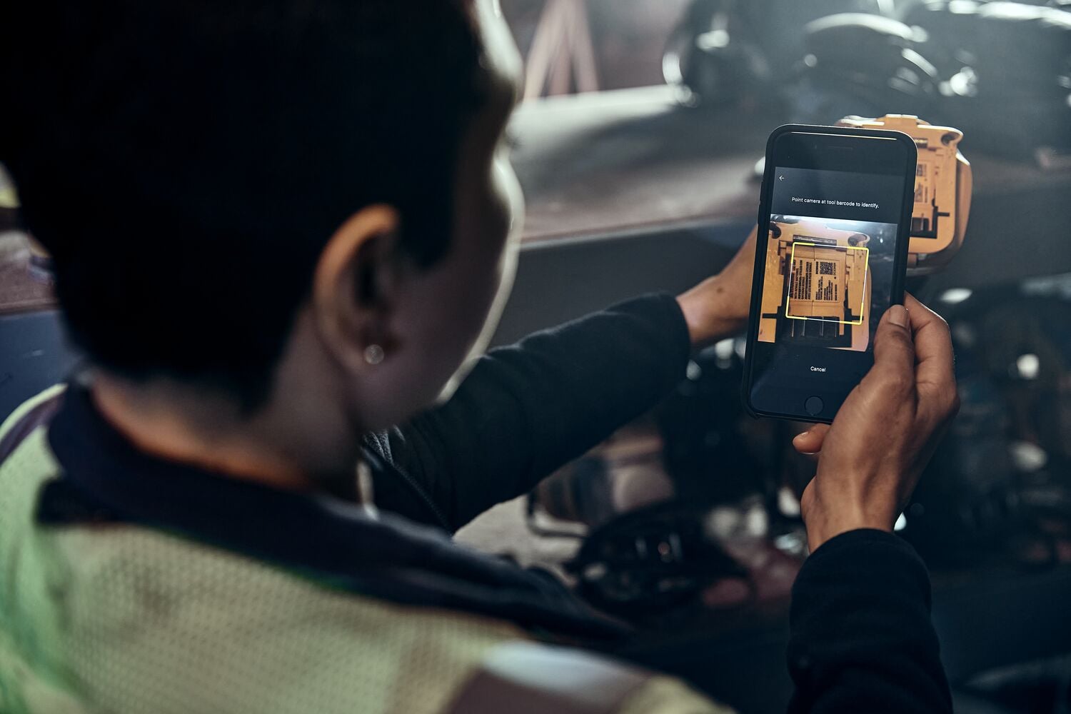 A person is using a smartphone to take a photo of a yellow DEWALT device in an industrial setting.